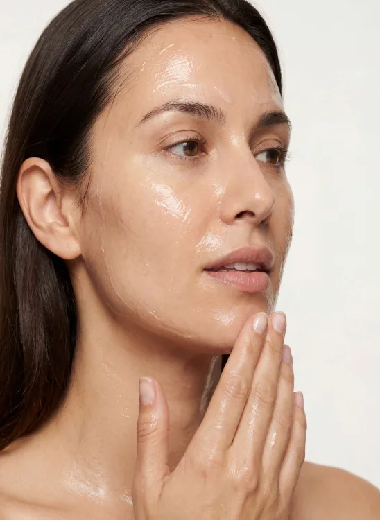 Skincare model applying cream to her cheek in natural light