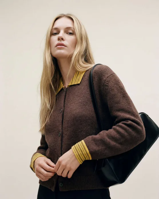 Blonde model in a brown knit cardigan carrying a black bag, studio portrait