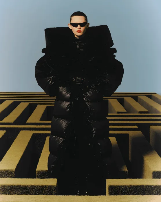 Figure in a black puffer outfit seated in a graphic yellow-striped set