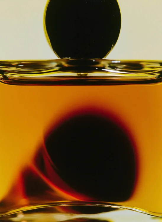 Amber perfume liquid in glass, backlit close-up
