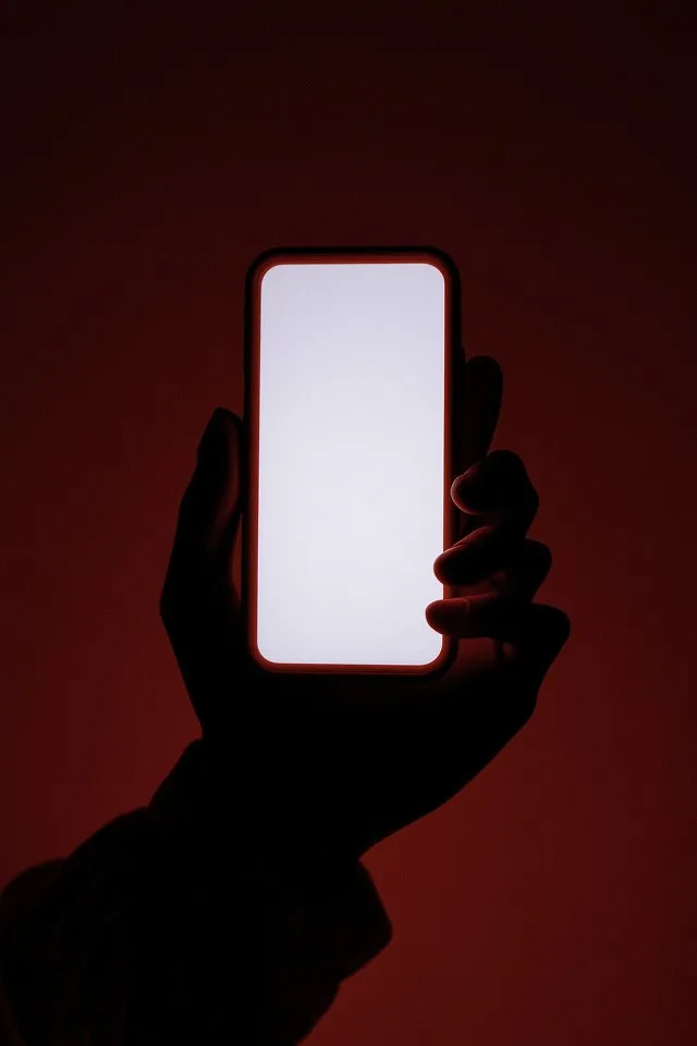 Hand holding a glowing white phone screen in red light